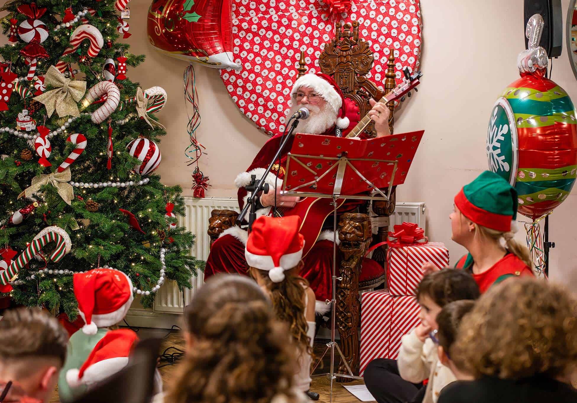 Santa Claus playing guitar at Valley View with children and Christmas decorations.